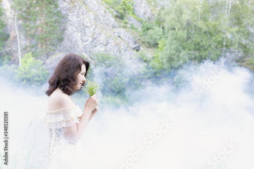 Beautiful girl with dark hair in fog with flowers.