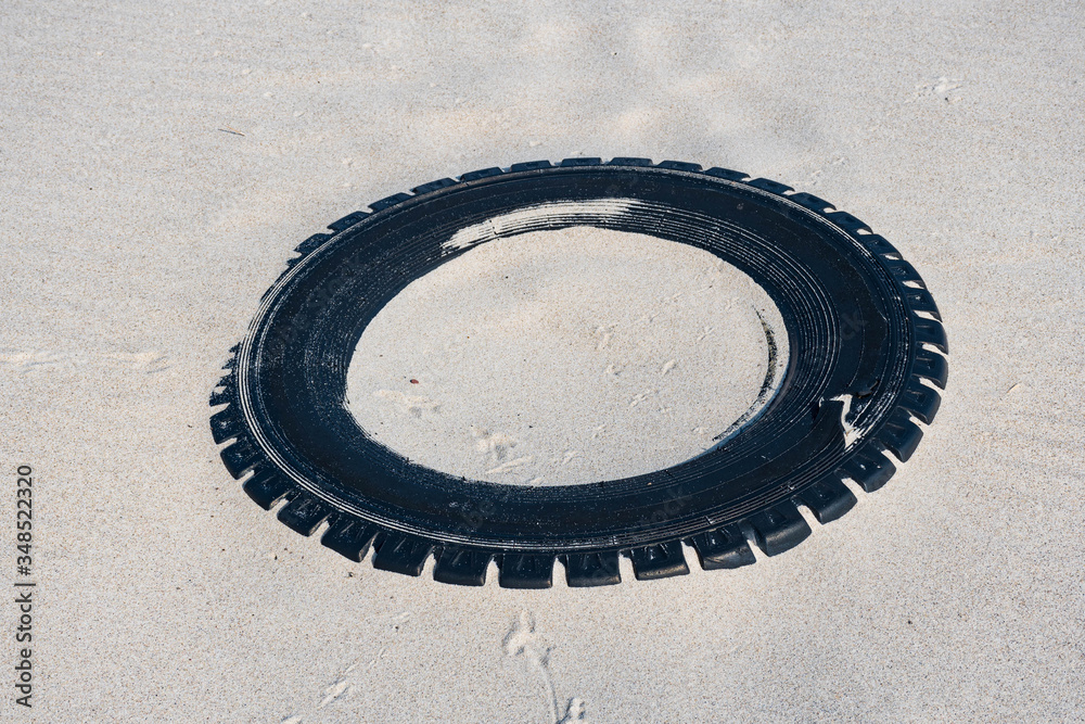 Big black rubber tire left on a sandy beach, environment pollution concept Big black rubber tire left on a sandy beach, environment pollution concept