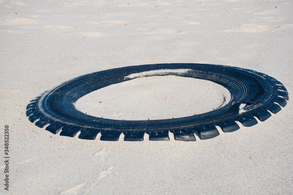 Big black rubber tire left on a sandy beach, environment pollution concept Big black rubber tire left on a sandy beach, environment pollution concept