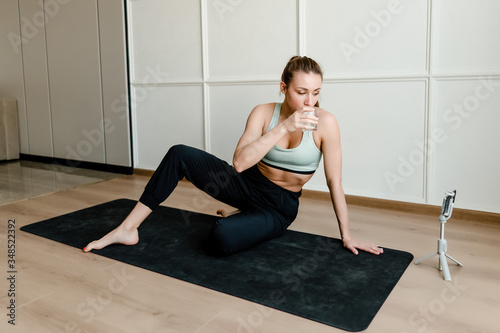 sporty woman sitting on yoga mat at home with phone online