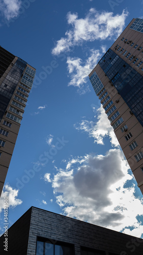 Blue sky with dark cloud betwen two high buildings. Roof tops under clouds