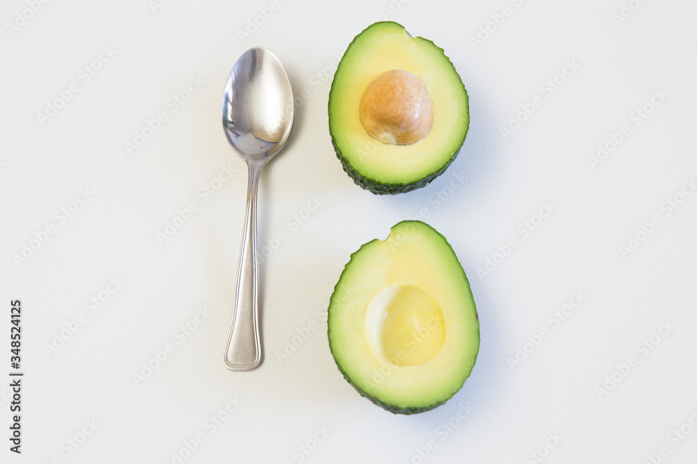Two halves of avocado with core and spoon. Top view. Isolated objects on white background. Fresh food or healthy diet concept Two halves of avocado with core and spoon. Top view. Isolated objects on white background. Fresh food or healthy diet concept