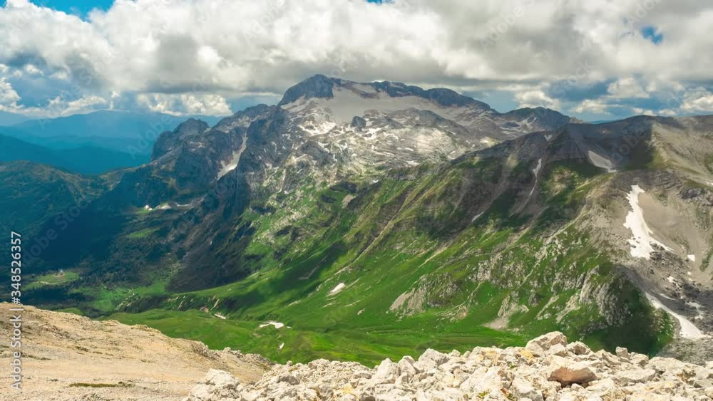 Stunning panoramic Timelapse of the beautiful large Adygea mountains, covered with snow and grass under huge cumulus clouds on a sunny spring day, Russia. nature view in a landscape of green valley.