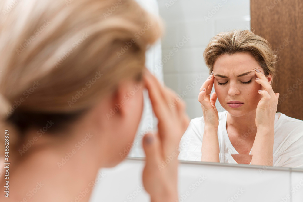 Woman looking in the mirror and having a headache Woman looking in the mirror and having a headache