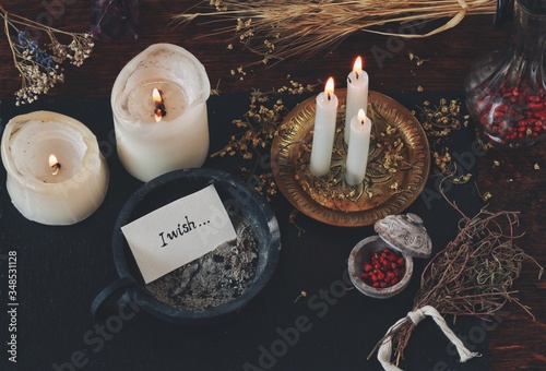 Peace of paper with words I wish written on it, put in cast iron candle holder with ashes in it, on wiccan witch altar. Casting a spell for wish to come true, manifesting. Burning candles, dried herbs