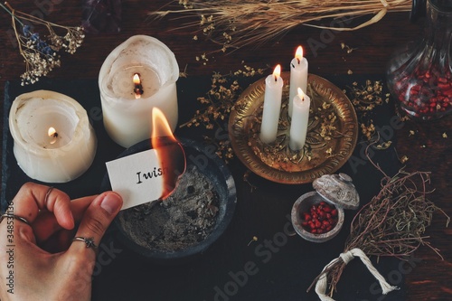 Female wiccan witch holding a burning peace of paper in her hand. White paper with I wish written on it. Casting a spell for wish to come true, sending thoughts into the Universe, dream manifestation photo