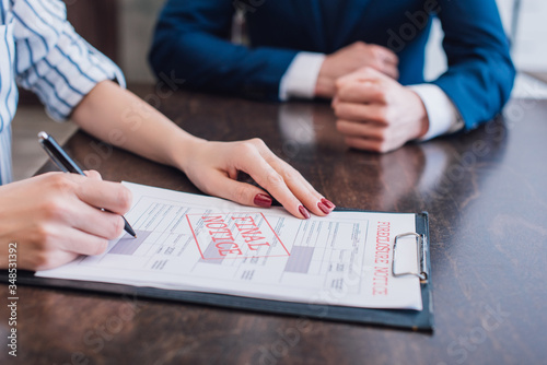 Cropped view of woman writing in documents with foreclosure and final notice near collector at table photo