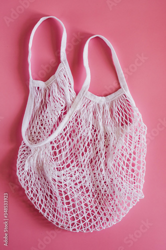 White cotton string knitted bag on pink background. Empty hand made bag. Zero waste, eco friendly shopping. Top view, flat lay. 