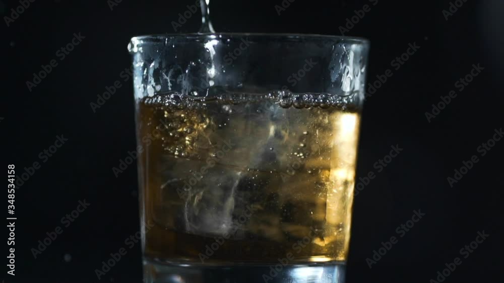 alcohol is poured to the glass with ice cubes in slow motion alcohol is poured to the glass with ice cubes in slow motion