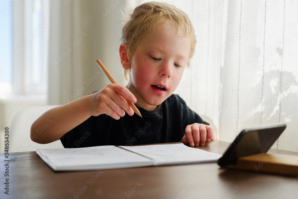 Little boy learning at home. Watching webinar by mobile, writing Little boy learning at home. Watching webinar by mobile, writing