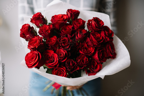 Fototapeta Naklejka Na Ścianę i Meble -  Very nice young woman holding big beautiful blossoming mono bouquet of fresh red roses wrapped in white paper on the grey wall background