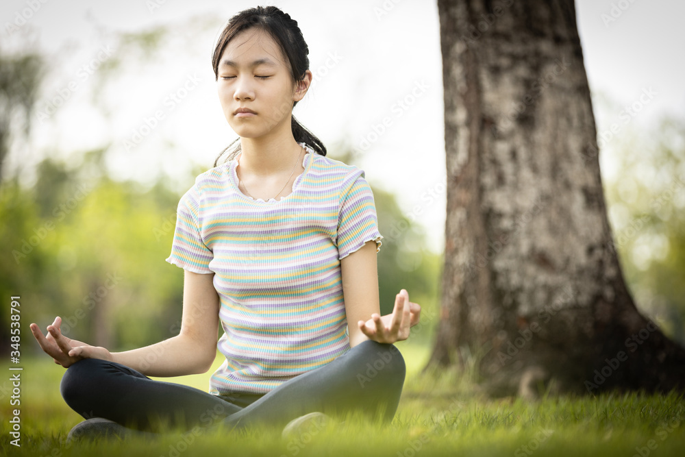 Happy woman meditating in yoga pose or lotus position on the green grass under the tree at park,asian child girl practicing yoga meditation in nature outdoor,relax time,calmness,meditation,health care Happy woman meditating in yoga pose or lotus position on the green grass under the tree at park,asian child girl practicing yoga meditation in nature outdoor,relax time,calmness,meditation,health care