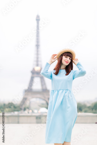 Beautiful young woman model wearing stylish hat and blue dress, posing in front of the Eiffel tower in Paris, France