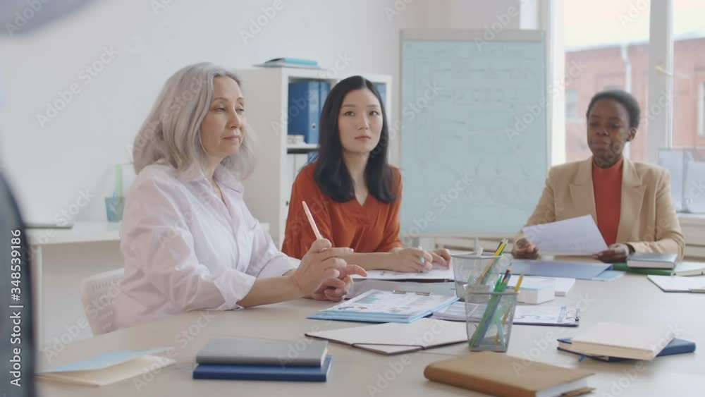Lockdown of three multiethnic businesswomen sitting at desk in the office and listening to unrecognizable speaker standing in front of them Lockdown of three multiethnic businesswomen sitting at desk in the office and listening to unrecognizable speaker standing in front of them