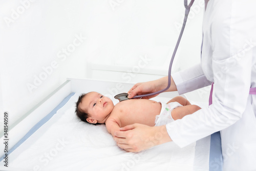 Doctor hand hold tiny Asian newborn baby sick sleeping during examine by pediatrician doctor with stethoscope, doctor monitoring heart pulse rate adorable infant in clinic, baby health care concept