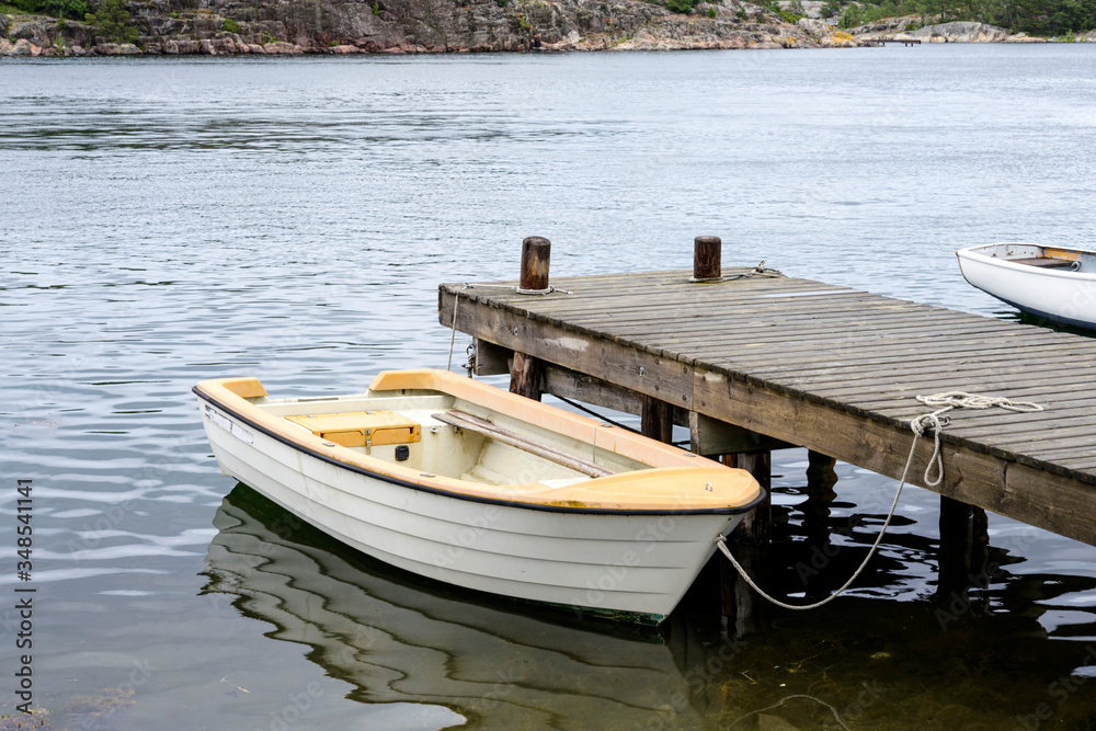 Wooden white boat parking on the wood pier on water with reflection background, Sweden.