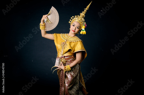 Beautiful Thai woman wearing traditional dancer dress headgear jewelry long nails holding fan dancing performance show on black background isolated.