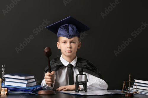 Portrait of little judge sitting at table against dark background photo