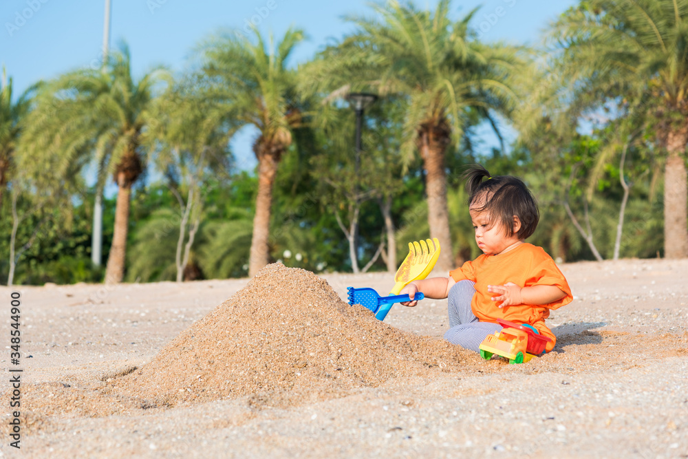Asian Thai happy cute little cheerful daughter girl funny digging playing toy with sand at an outdoor tropical beach in summer day with copy space Asian Thai happy cute little cheerful daughter girl funny digging playing toy with sand at an outdoor tropical beach in summer day with copy space