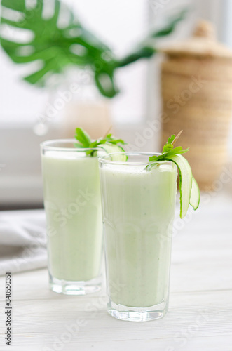 Refreshing fermented milk drink with cucumber and herbs. Two with such a cocktail in a light interior on a white table.