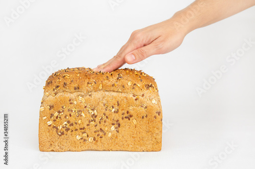 Hand pushing soft brick form bread with fingers. Fresh loaf with cereals, oats, seeds isolated on white background. Studio shot. Side view. Homemade bakery and nutrition concept