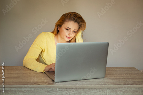 Young woman is working online. Girl with laptop. Smiling woman in a yellow cardigan