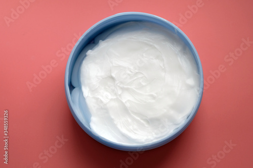 White cream in a round container top view. Body cream in a box on a pink background. Face and body skin care, cosmetic products.