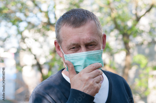 Portrait of mid age european man with surgery face mask on backyard background in sunny spring day