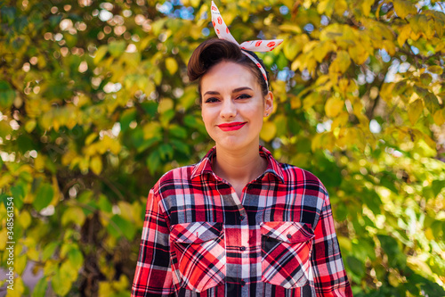 Beautiful woman with make up and hair in pin up style standing next to the autumn bush photo