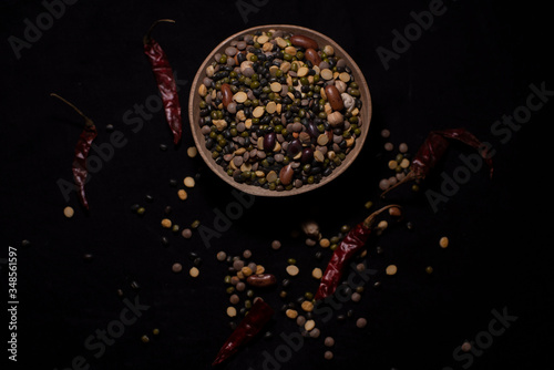 Top down image of a bowl of Indian mixed pulses decorated with cereals and dried chilli in a dark copy space background. Food and product photography.