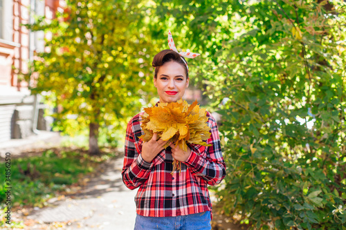 Beautiful woman with make up and hair in pin up style holding big bouquet of maple yellow leaves.