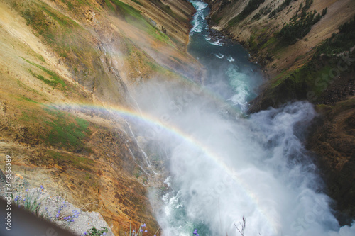 Close up picture of double rainbow in the steam from waterfall in Grand Yellowstone canyon in national park United States. River view between orange hills and green grass on the hill  nature concept