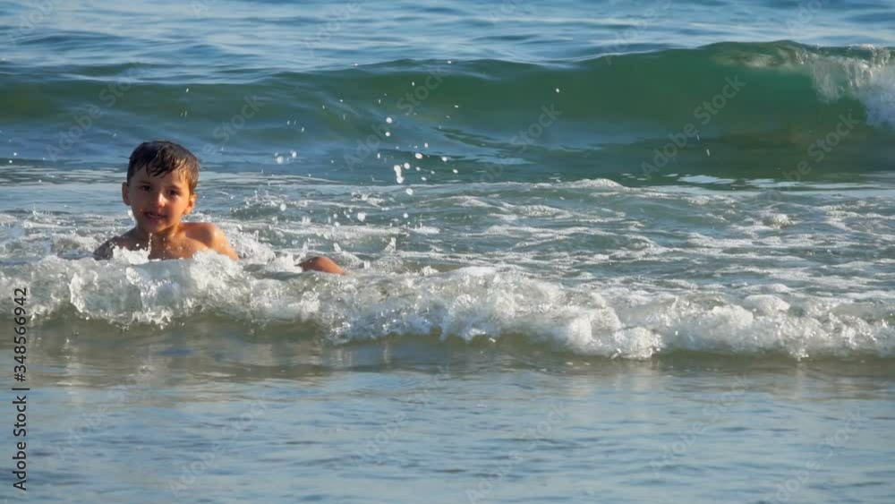 Happy cheerfull little boy is jumping in the sea water at the line of the sea surf. Sunny summer day at the sea. Happy cheerfull little boy is jumping in the sea water at the line of the sea surf. Sunny summer day at the sea.