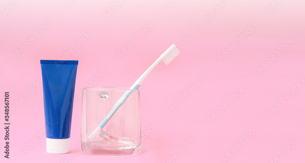 Blue toothpaste tube and toothbrush in transparent glass with gradient lighting on pastel pink background, close up with copy space Blue toothpaste tube and toothbrush in transparent glass with gradient lighting on pastel pink background, close up with copy space
