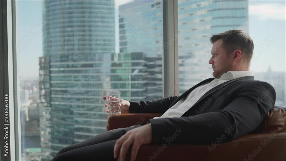 A young businessman is sitting in a chair with a glass of water. Young businessman works sitting in the office and thinks. 