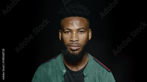 Young african man looking serious. African man with beard looking at camera on black background.
