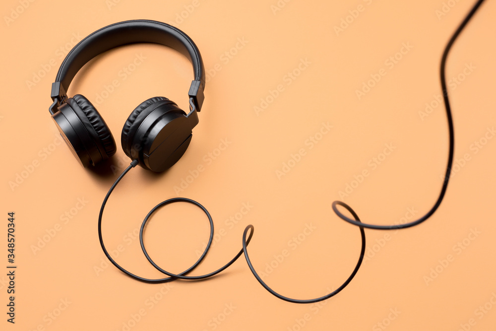 Photo of stylish modern black headphones over beige background.