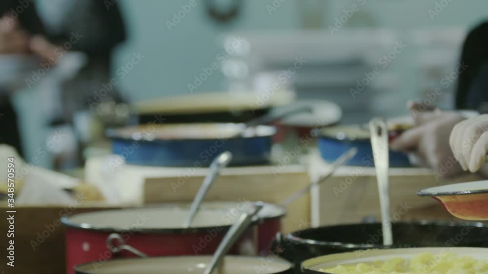 People getting food in plates in a kitchen's buffet serving line - slow motion People getting food in plates in a kitchen's buffet serving line - slow motion