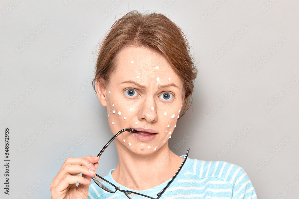 Portrait of puzzled girl with white drops of face cream on skin Portrait of puzzled girl with white drops of face cream on skin