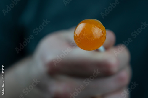 Orange candy on a stick in a hand on a dark background