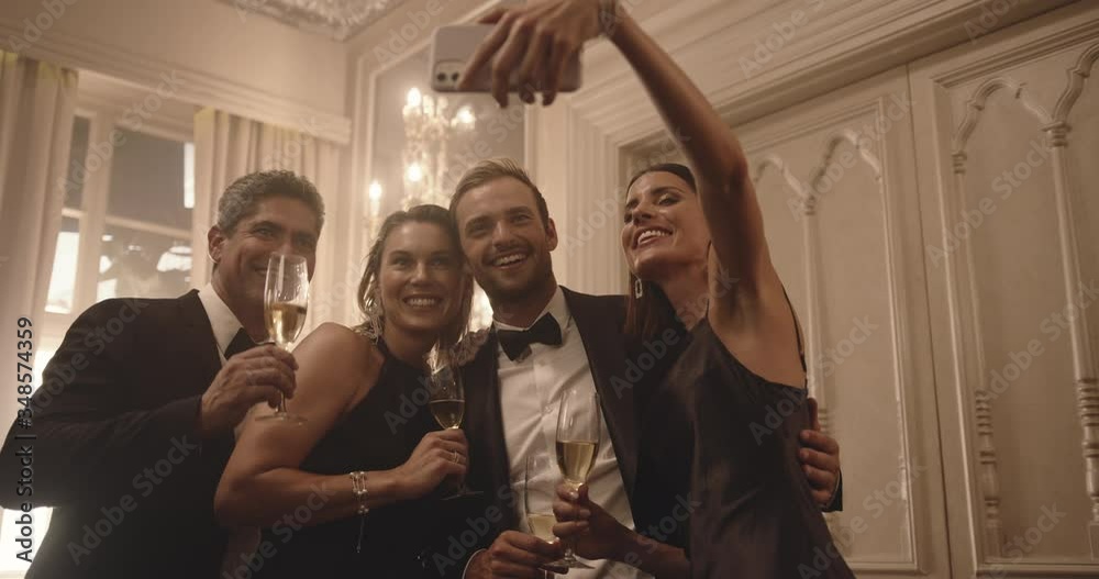 Woman taking selfie with friends at gala night. Two couple enjoying a party and taking selfie with mobile phone.
