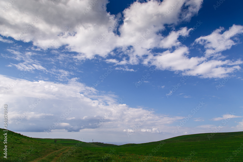 Cumulus clouds on a blue sky. Over the green field. Spring flowering grass. Summer natural background
