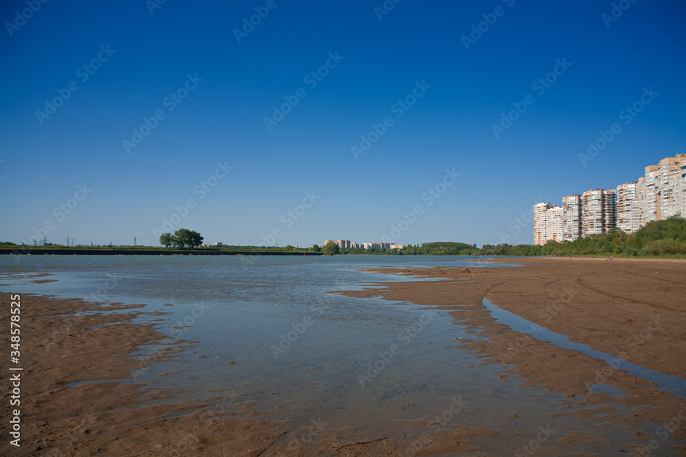 border of a large multi-story city and countryside. tall houses on the banks of a shallow river. the concept of urban expansion and the destruction of small rural settlements