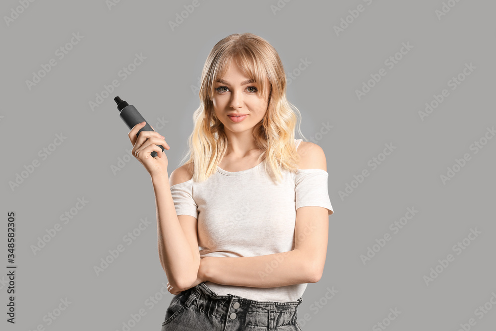 Beautiful young woman with hair spray on grey background Beautiful young woman with hair spray on grey background