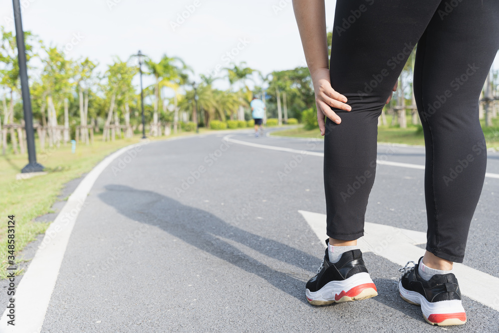 Asian woman use hands hold on her knee injury while running on road in the park, Injury from workout concept.