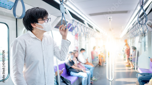 Asian man wearing surgical face mask holding handrail on skytrain or urban train. Coronavirus (COVID-19) outbreak prevention in public transportation. Health awareness for pandemic protection © zephyr_p