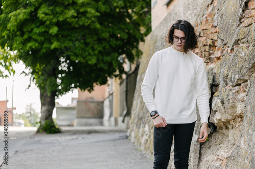 Man wearing white sweatshirt or hoodie and glasses outside on the city streets. Sweatshirt or hoodie for mock up, logo designs or design prints with free space.