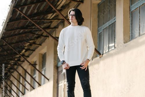 Man wearing white sweatshirt or hoodie and glasses outside on the city streets. Sweatshirt or hoodie for mock up, logo designs or design prints with free space.