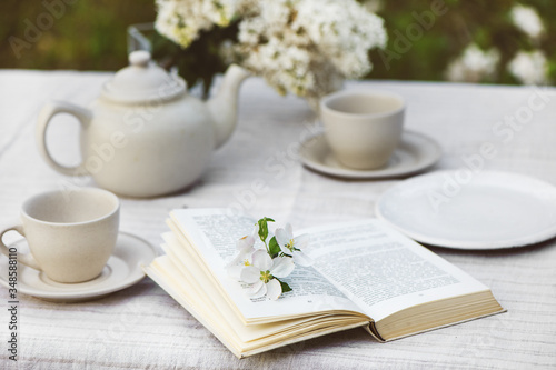 Open book with flowers, tea cups, tea pot and branch of lilac.