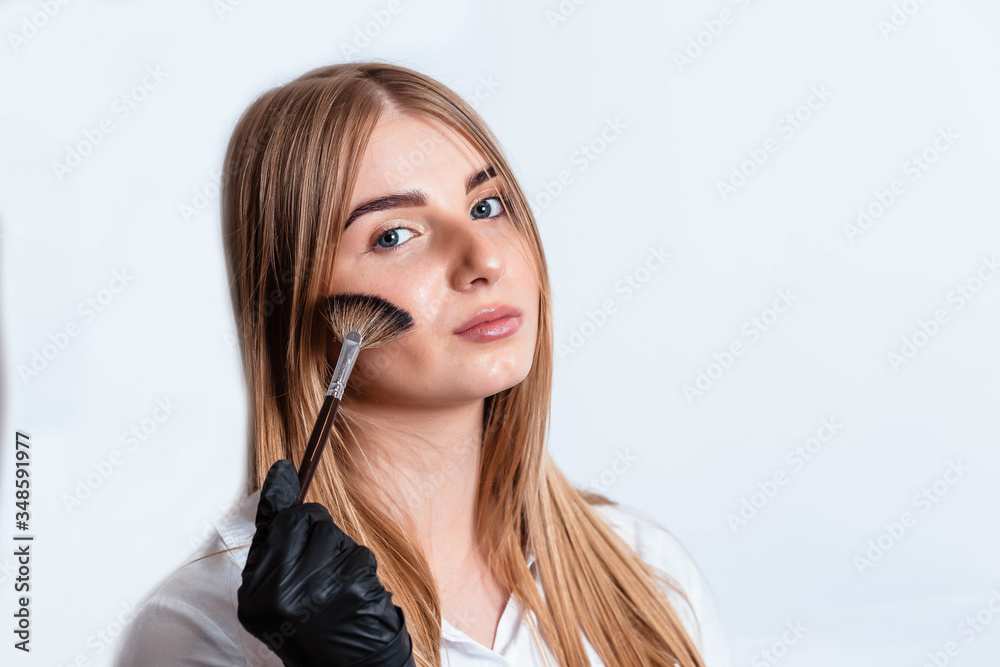 Beautiful young woman doing makeup. Girl with a brush in hand to apply powder on the face. Woman in black gloves makes makeup. Woman makes makeup herself on a white background. Beautiful young woman doing makeup. Girl with a brush in hand to apply powder on the face. Woman in black gloves makes makeup. Woman makes makeup herself on a white background.